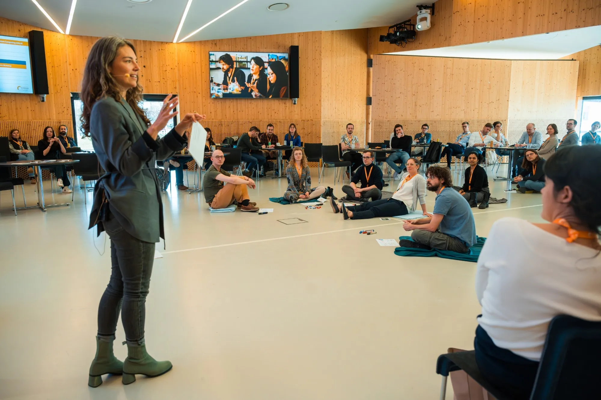 Lena Tünkers moderiert einen Workshop, die Teilnehmenden sitzen im Kreis auf dem Boden